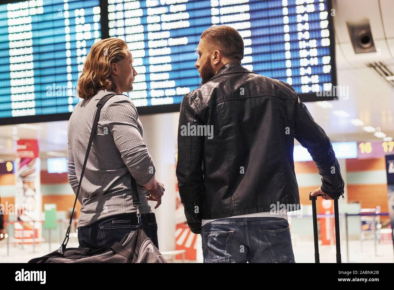 Foto de dos compañeros de situar en el aeropuerto cerca de sistema de visualización de la información de vuelo Foto de stock