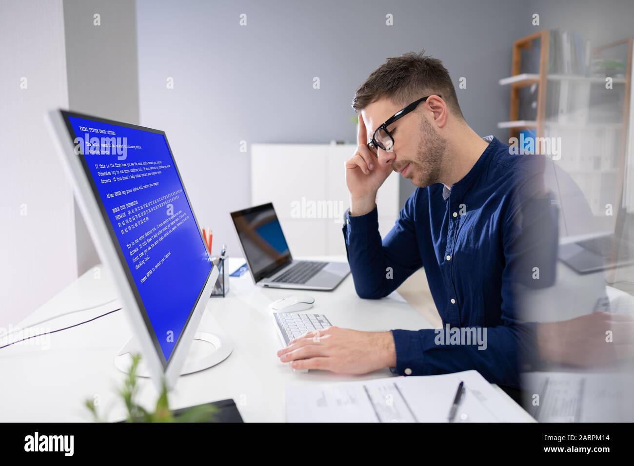 Preocupa al hombre en Ordenador con pantalla de fallo del sistema en el lugar de trabajo Foto de stock