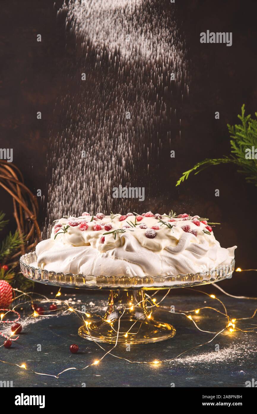 Pavlova postre en la forma de una guirnalda de navidad decorado con arándanos rojos y verdes de romero. Azúcar glas en polvo. Año nuevo las luces festivas. Foto de stock