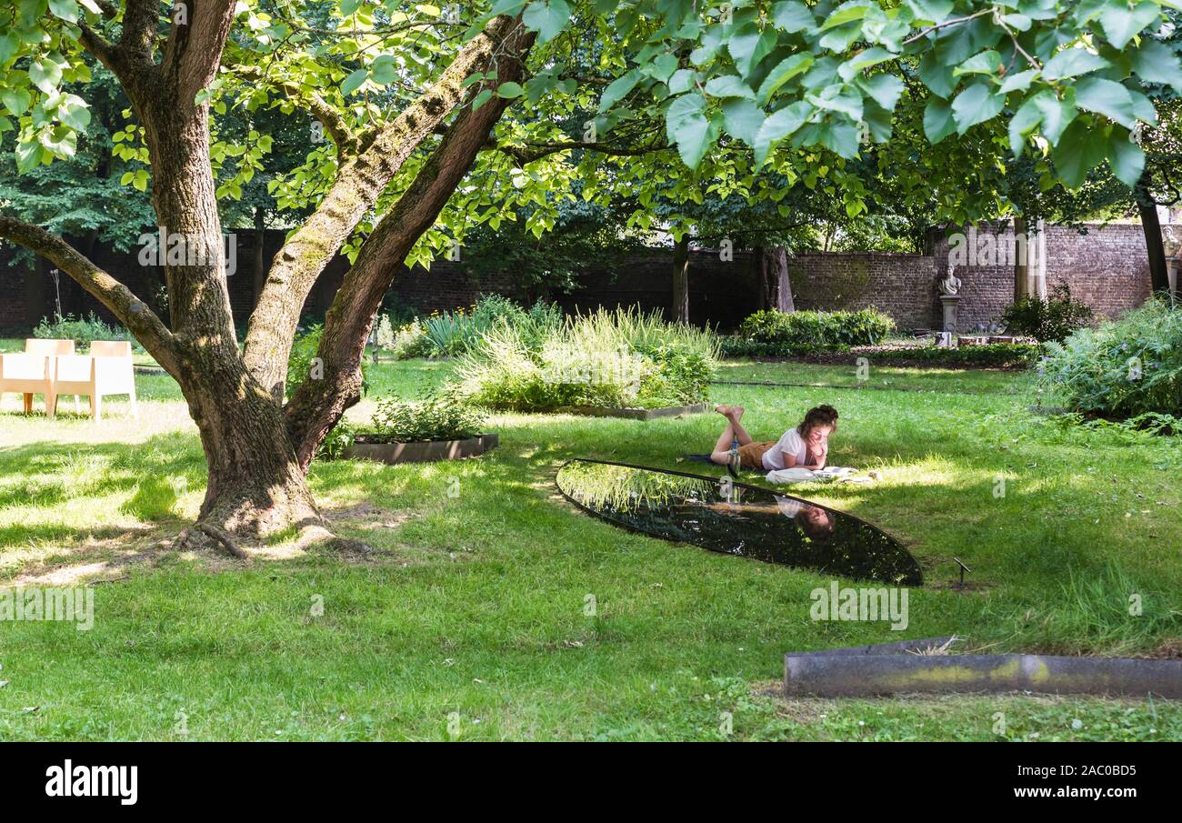 Anderlecht, Bruselas / Bélgica - 06 26 2019: atractivo joven en ropa de verano leyendo en el verde césped, tumbado sobre su barriga Foto de stock