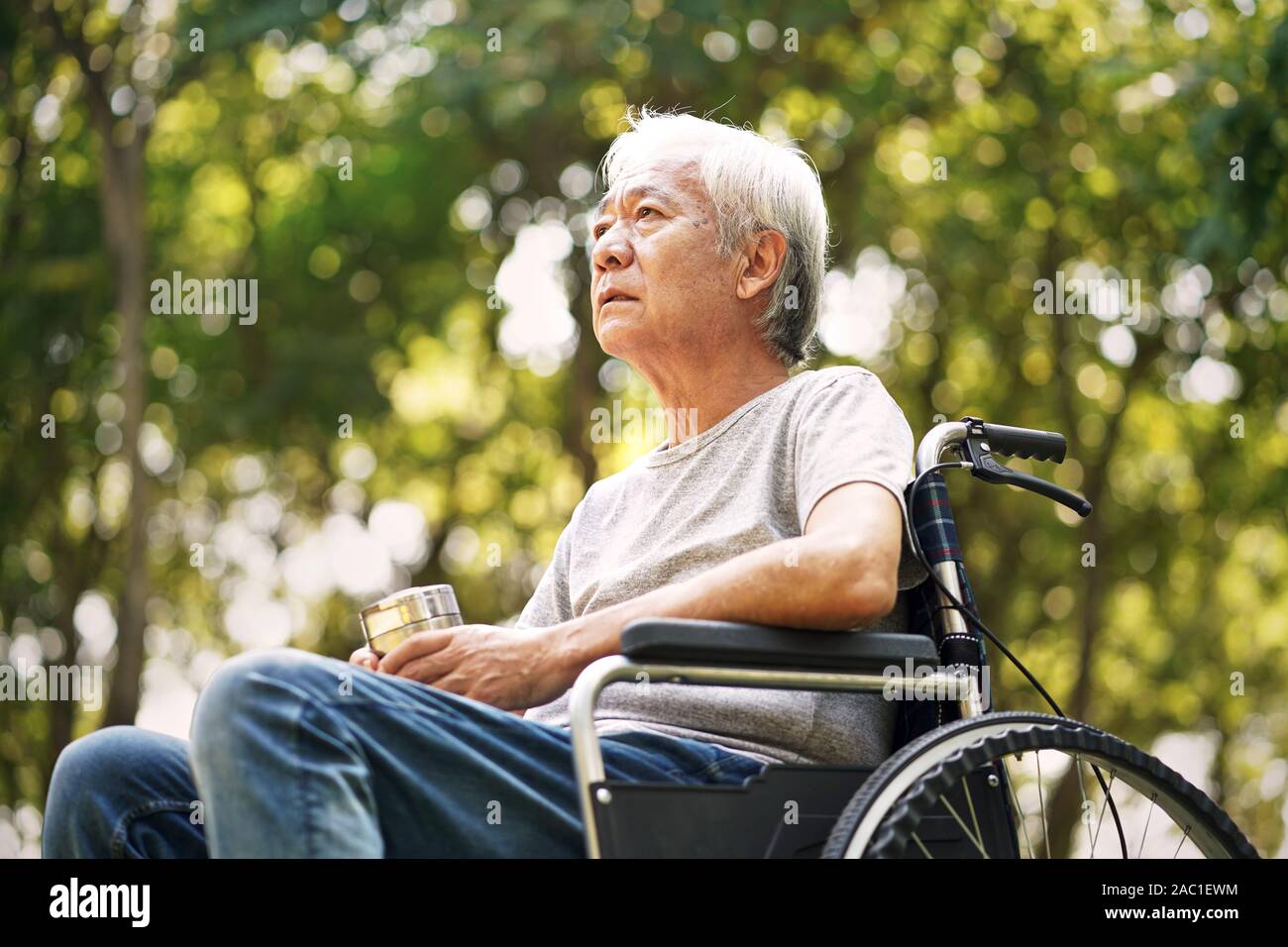 Asian anciano sentado en una silla de ruedas mirando triste y deprimida Foto de stock