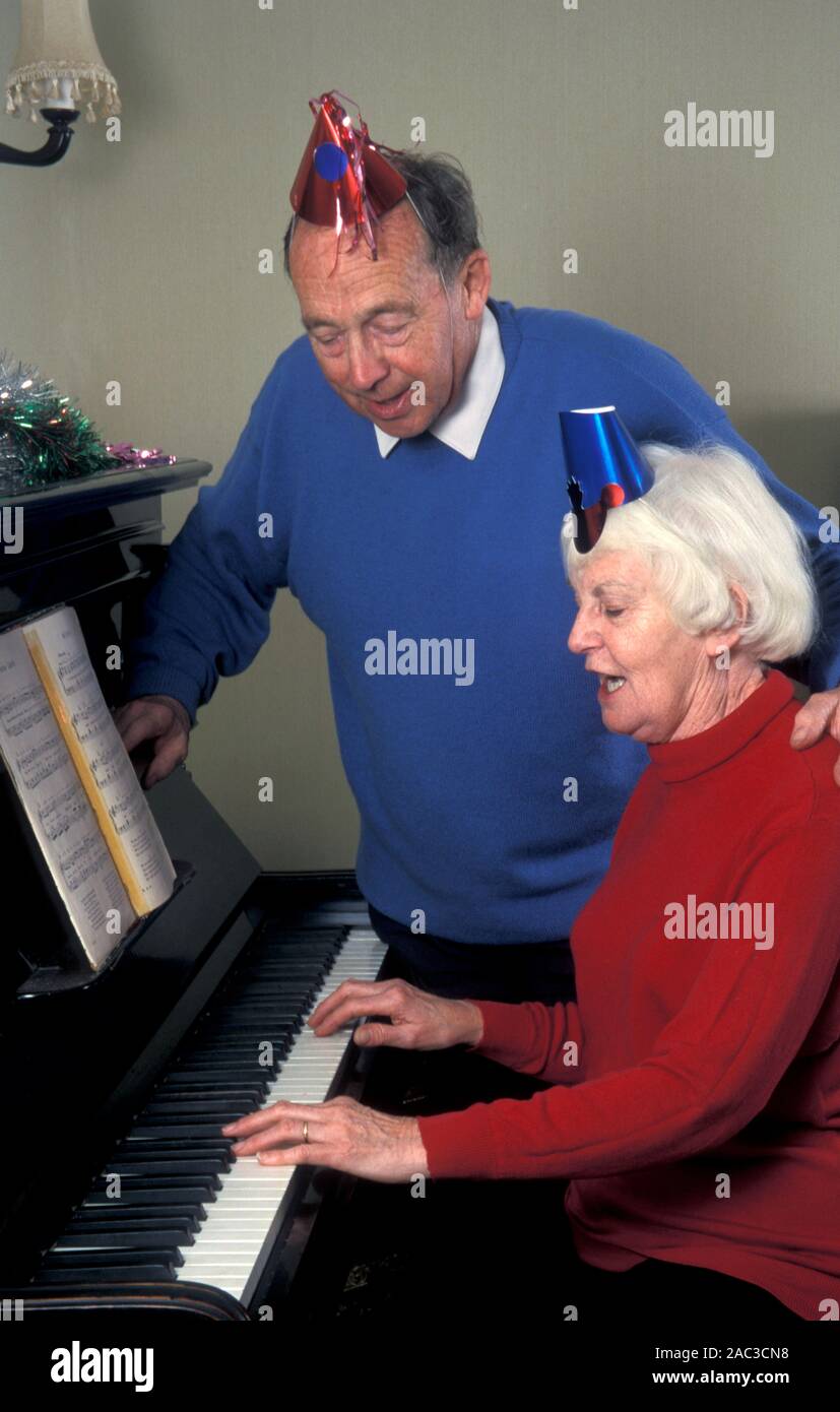 Las parejas ancianas en sombreros de fiesta tras cantar la canción de piano alrededor en Navidad Foto de stock