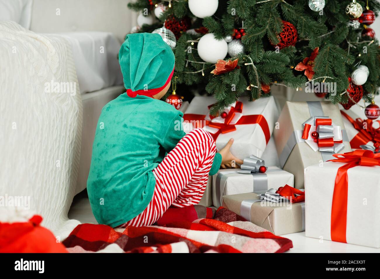 Boy abrir los regalos bajo el árbol de Noël en mañana. Niñito muchacho  sentado en el suelo abriendo regalos de Navidad. Niño bajo el árbol de  Navidad con cajas de regalo. Deco