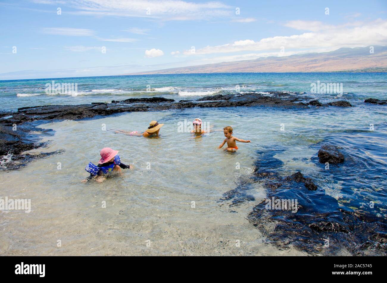 Una niña con el brazo floaties juega con un joven, mientras sus madres mirar en una piscina de marea en Puako, South Kohala, Isla Grande. Foto de stock
