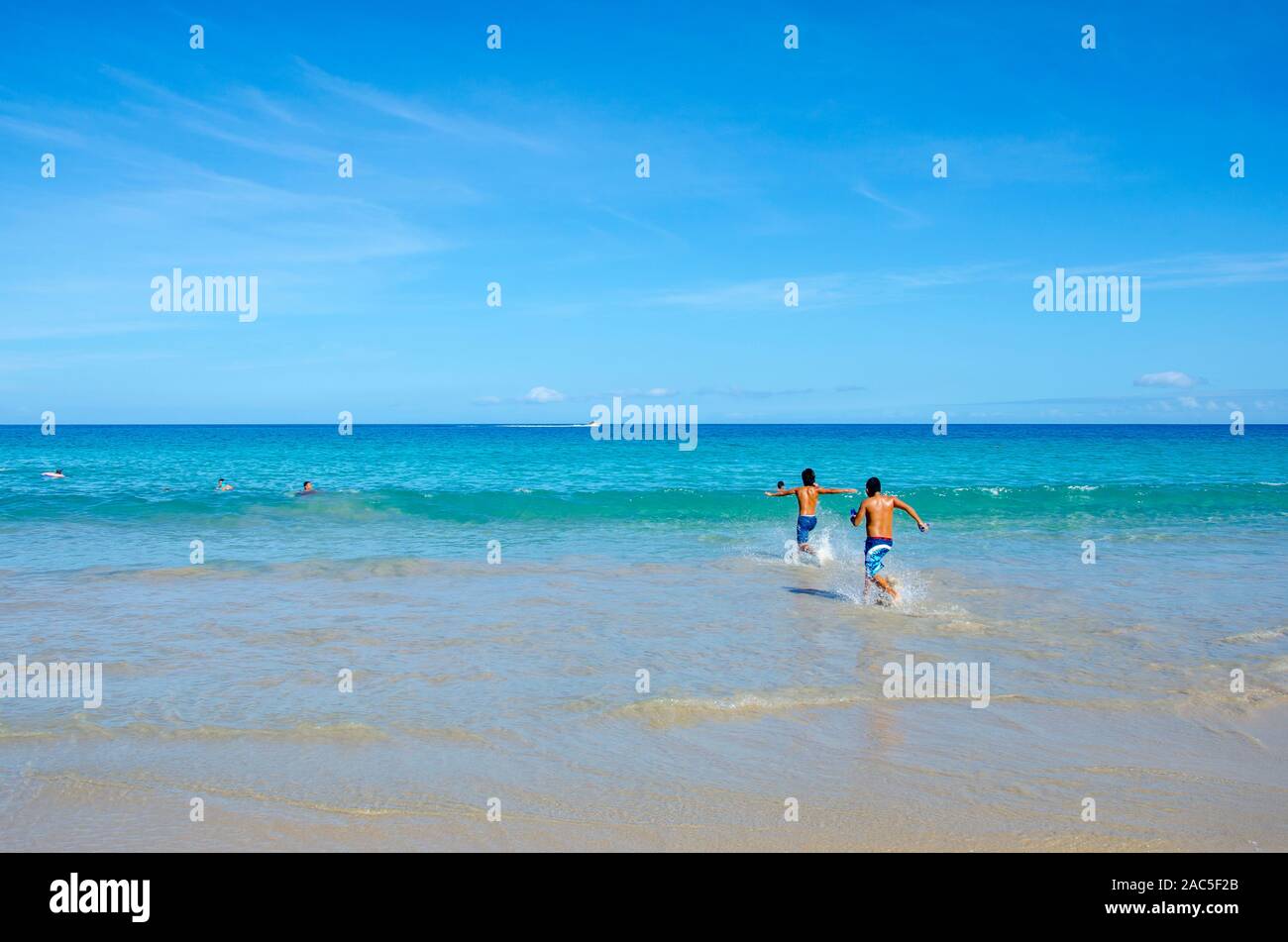 Dos muchachos adolescentes corriendo hacia el océano en Hapuna Beach, a lo largo de la costa Kohala de la Isla Grande. Esta playa de arena blanca ha sido calificado como uno de los mejores bea Foto de stock