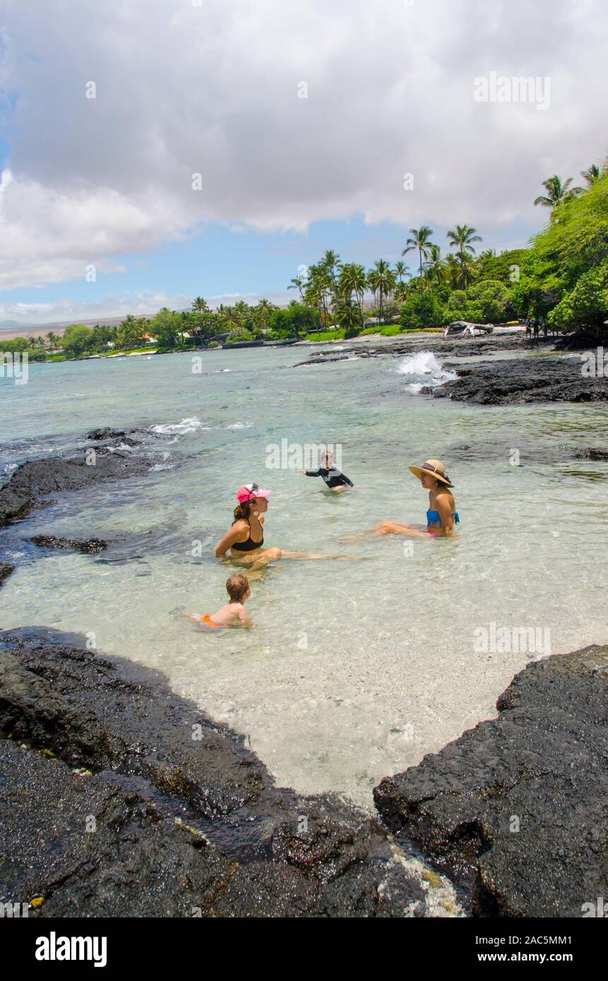 Dos niños locales y sus madres disfrutar de una piscina natural en una playa en Puako en un día soleado, South Kohala, Isla Grande. Foto de stock