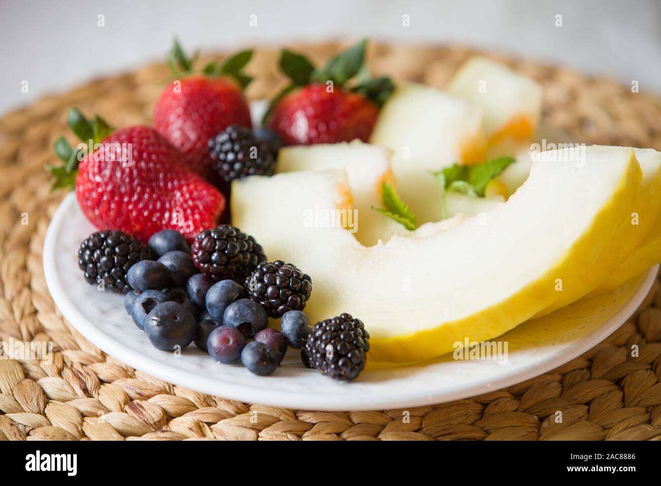 Melón cortado y bayas. Ensalada de frutas de fresas, arándanos, melón, menta y moras. Dieta ensalada en la placa blanca - desayuno, pérdida de peso. Foto de stock