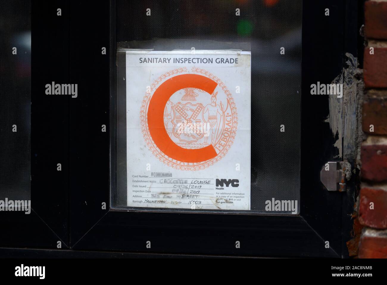Una inspección sanitaria de NYC la letra 'C' grado adhesivo en un establecimiento de alimentos con información de identificación redacted Foto de stock