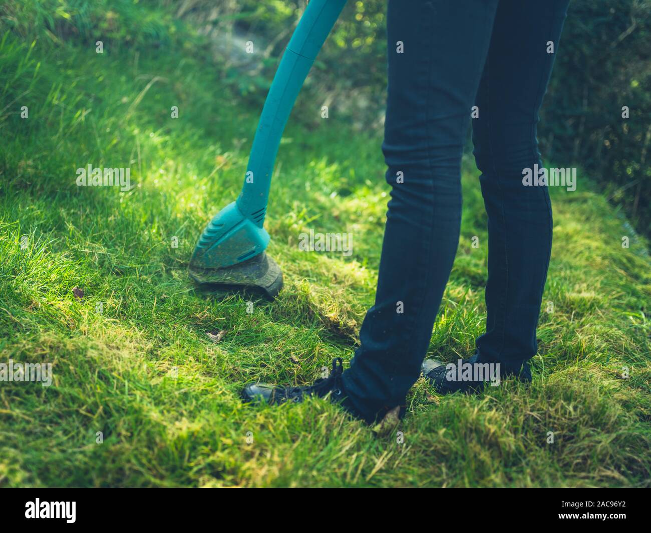 Una mujer joven está cortando el césped utilizando una hierba strimmer Foto de stock