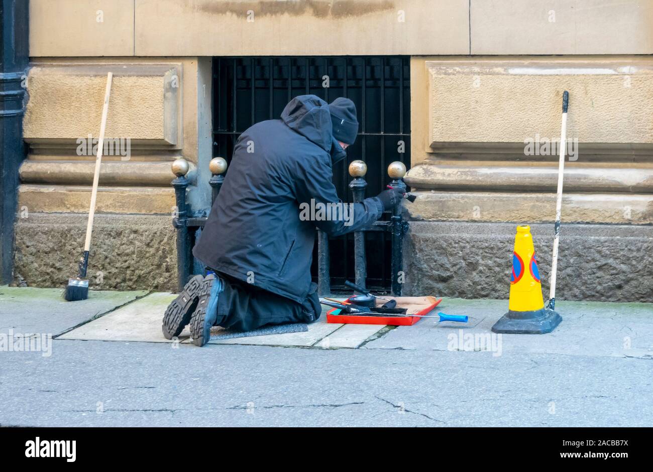 Trabajador masculino senior de rodillas para retocar la pintura negra en un metal ventanas enrejadas en Liverpool Foto de stock