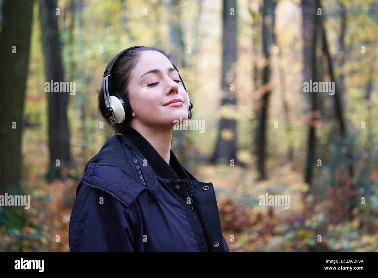 Mujer joven en su 20s al escuchar música con auriculares inalámbricos en franca forest - estilo de vida al aire libre en otoño, con espacio de copia Foto de stock