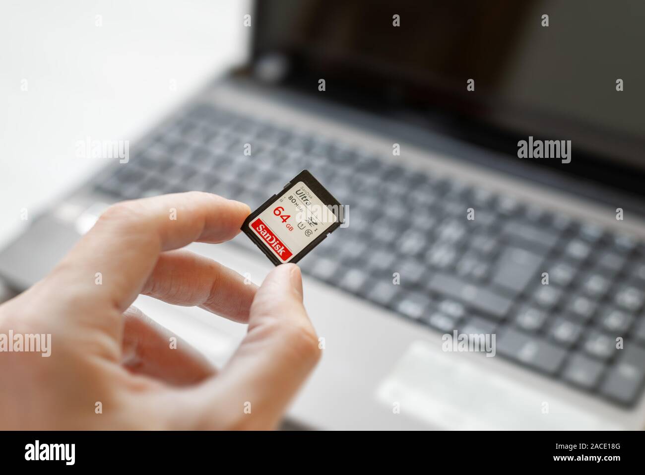 Mano sujetando 64 GB Tarjeta SD por encima de un equipo portátil. Concepto de transferencia de fotos y vídeos desde una tarjeta a un ordenador Foto de stock