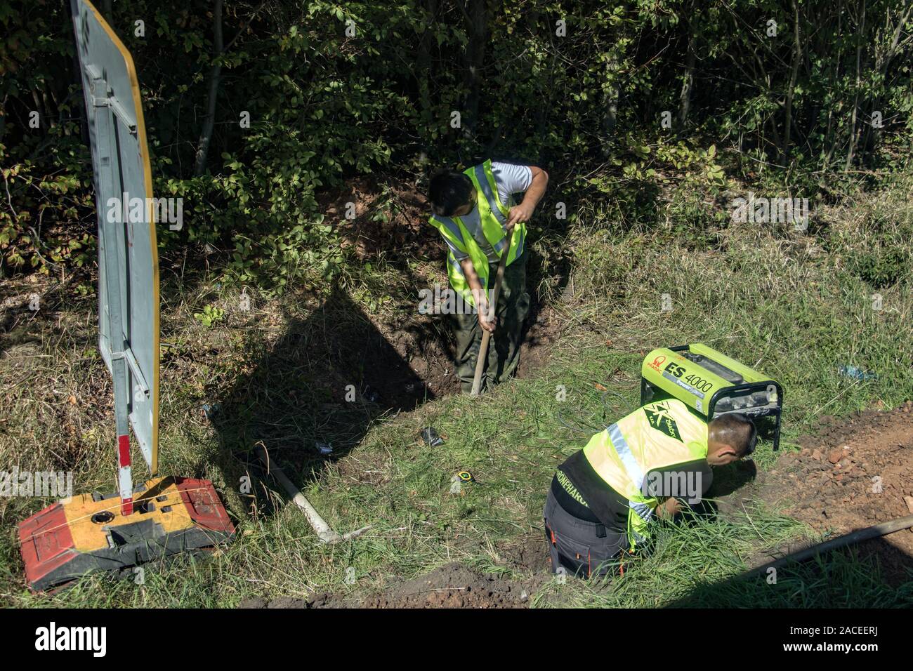Chequia Central, República Checa, 04 SEP 2019, Equipo de trabajadores con chaleco reflectante cavando hoyos al lado de una carretera. Trabajos manuales pesados sobre piscina c Foto de stock