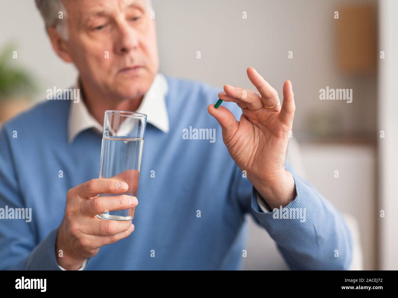 Anciano sosteniendo una píldora y vaso de agua interiores Foto de stock