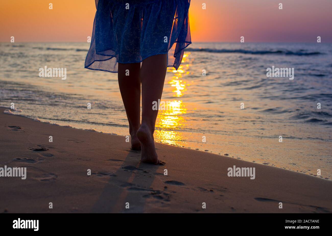 Primer plano de la mujer pies caminando por la playa durante una colorida puesta de sol. Mujer caminando hacia el mar, la parte del cuerpo, las piernas de las mujeres perfectas, disfrutar del tiempo Foto de stock