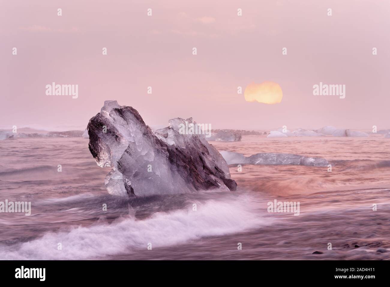 Bloques de hielo en una playa de fuerte oleaje, el agua en movimiento puede ser visto (larga exposición, trazas de movimiento), una gran puesta de sol Foto de stock