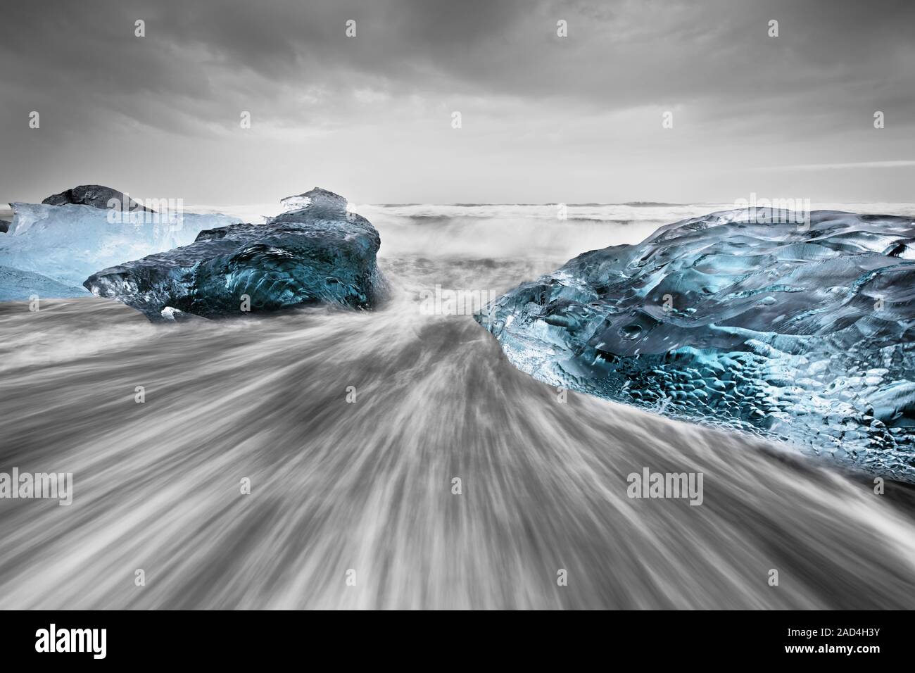 Bloques de hielo en los tonos azules en una playa negra con fuerte oleaje, el agua en movimiento puede ser visto (larga exposición, restos claros de movimiento). Foto de stock