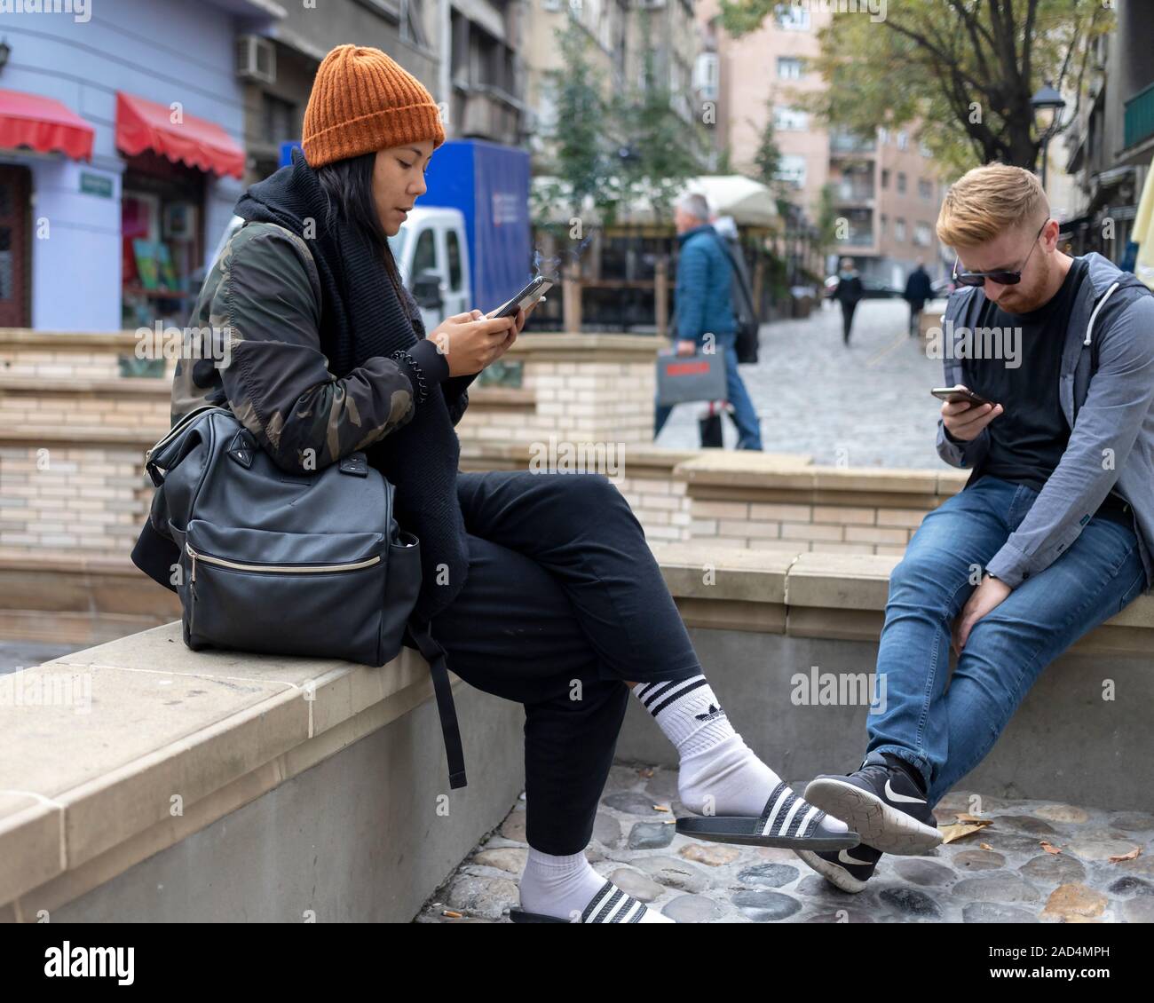 Belgrado, Serbia, Oct 7, 2019: una joven pareja sentada en la calle se centró en sus smartphones Foto de stock
