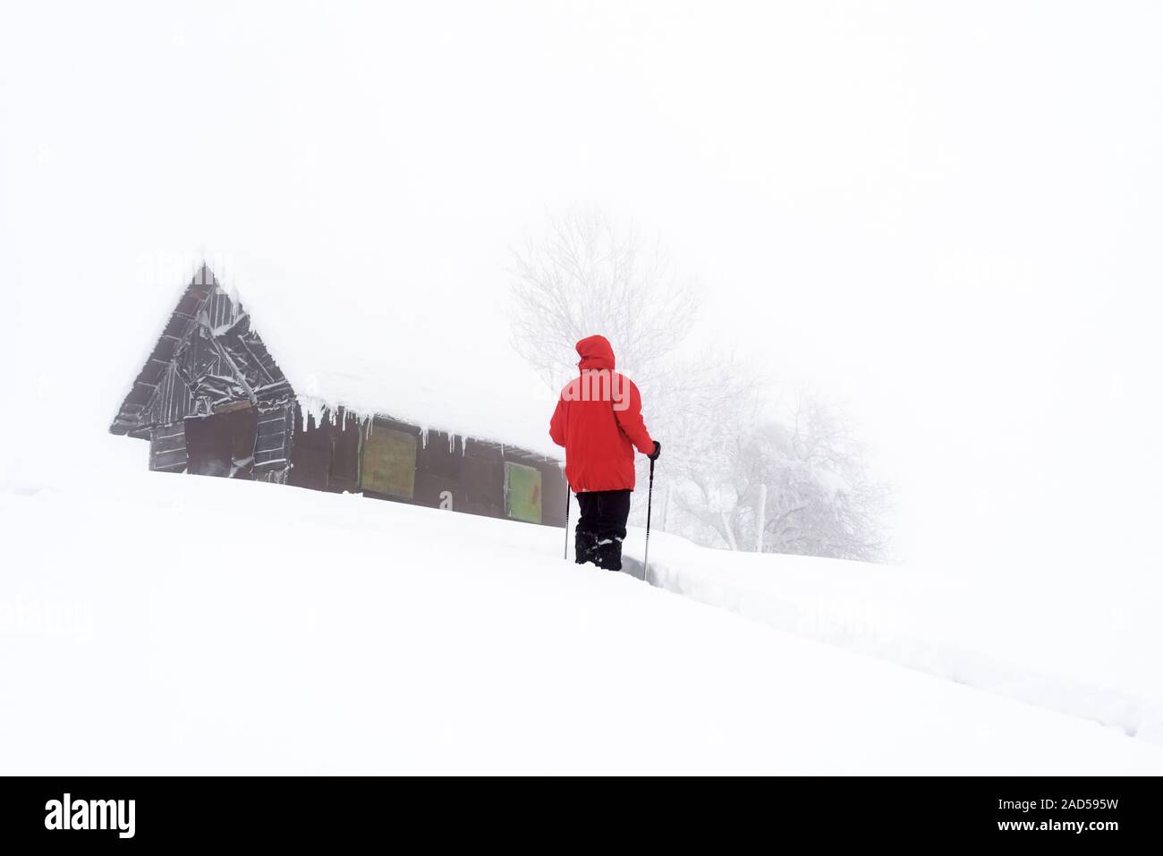 Paisaje invernal minimalista con casa de madera y turista en montañas nevadas. Weater nublado, fotografía paisajística Foto de stock
