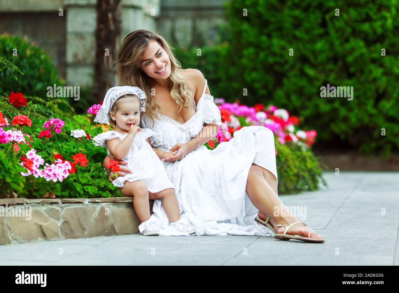 Hermosa joven mamá está sentada con su hija en el parque. Vestidos blancos.  Son felices y riendo. Agradable clima cálido Fotografía de stock - Alamy