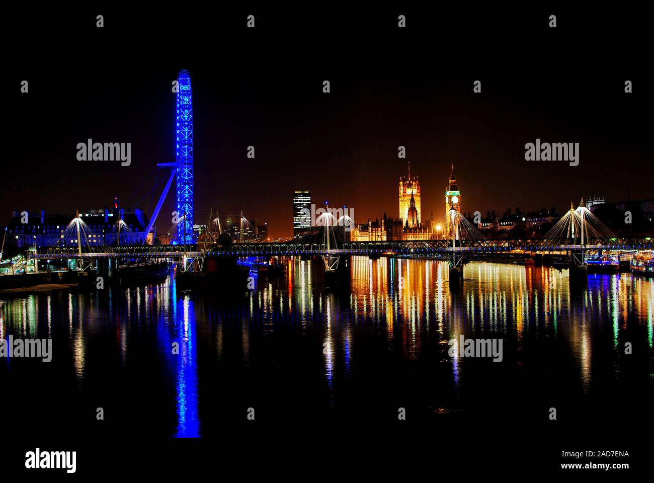 Una vista nocturna del puente Hungerford desde Waterloo Bridge con el London Eye y la Abadía de Westminster en el horizonte y se refleja en el río Támesis. Foto de stock