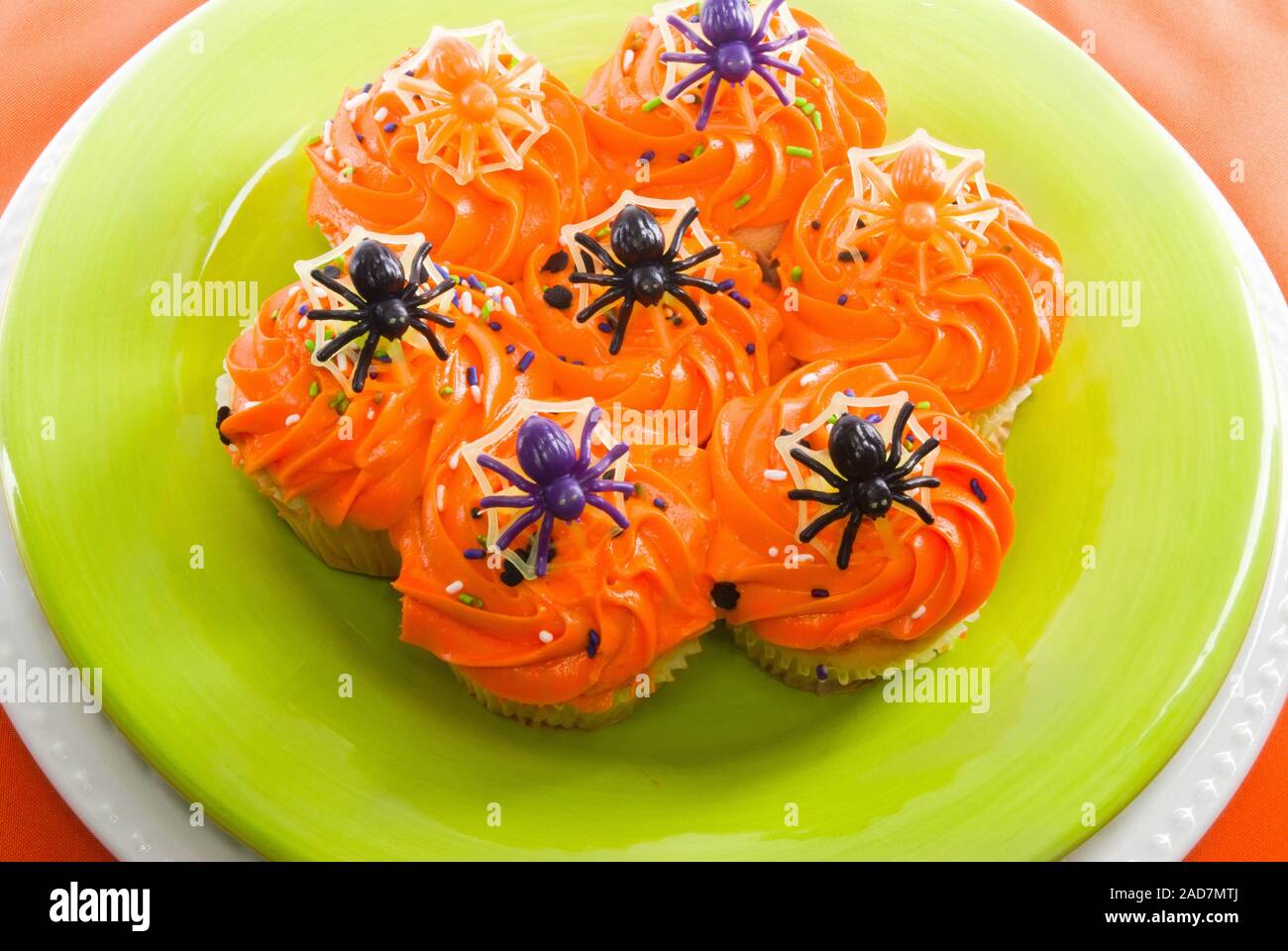 Colorido Halloween cupcakes decoradas con arañas de plástico de juguete verde lima, servido en un plato con un fondo de color naranja. Foto de stock