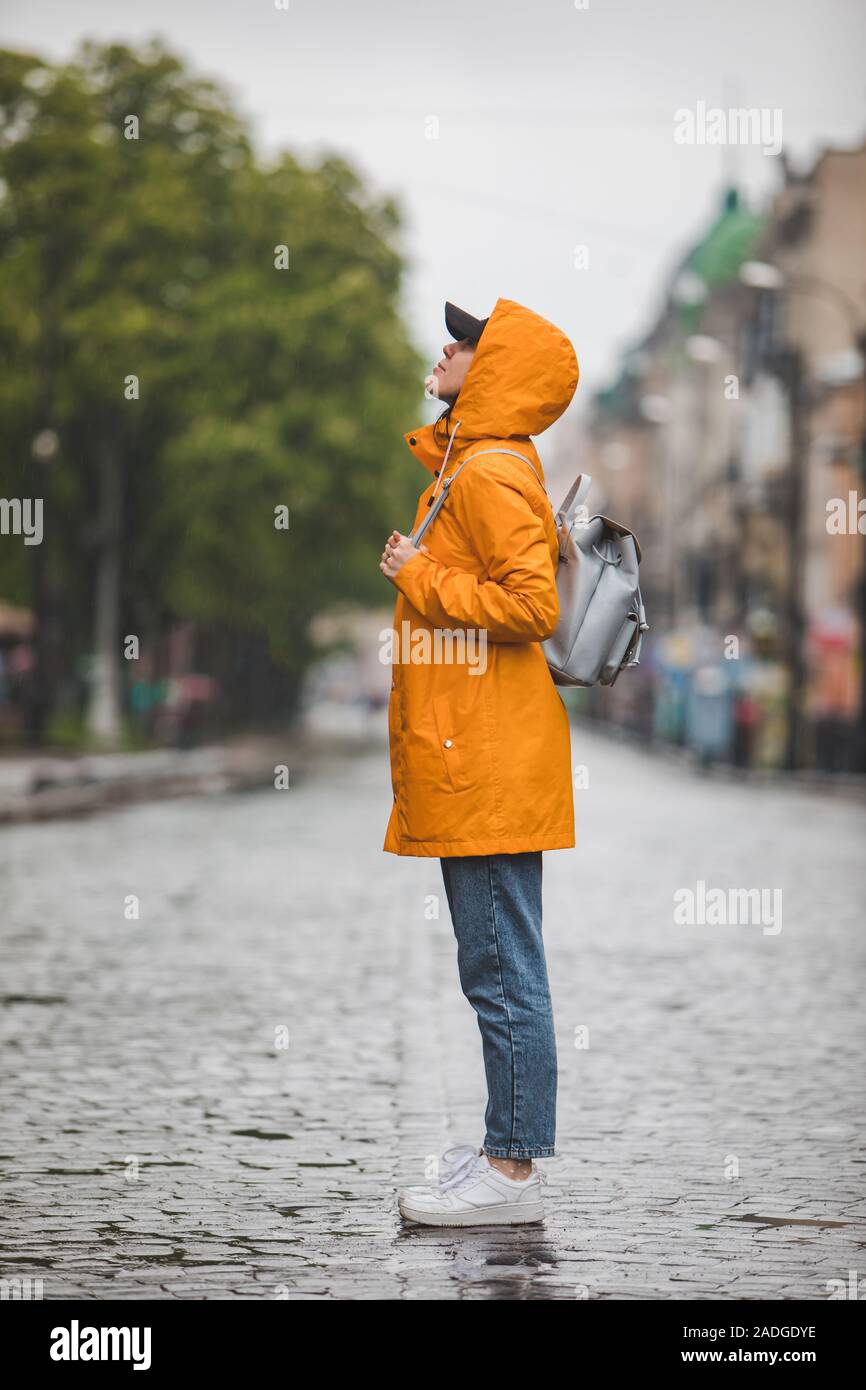 Vista lateral de la mujer en amarillo impermeable de pie en las calles de la ciudad Foto de stock