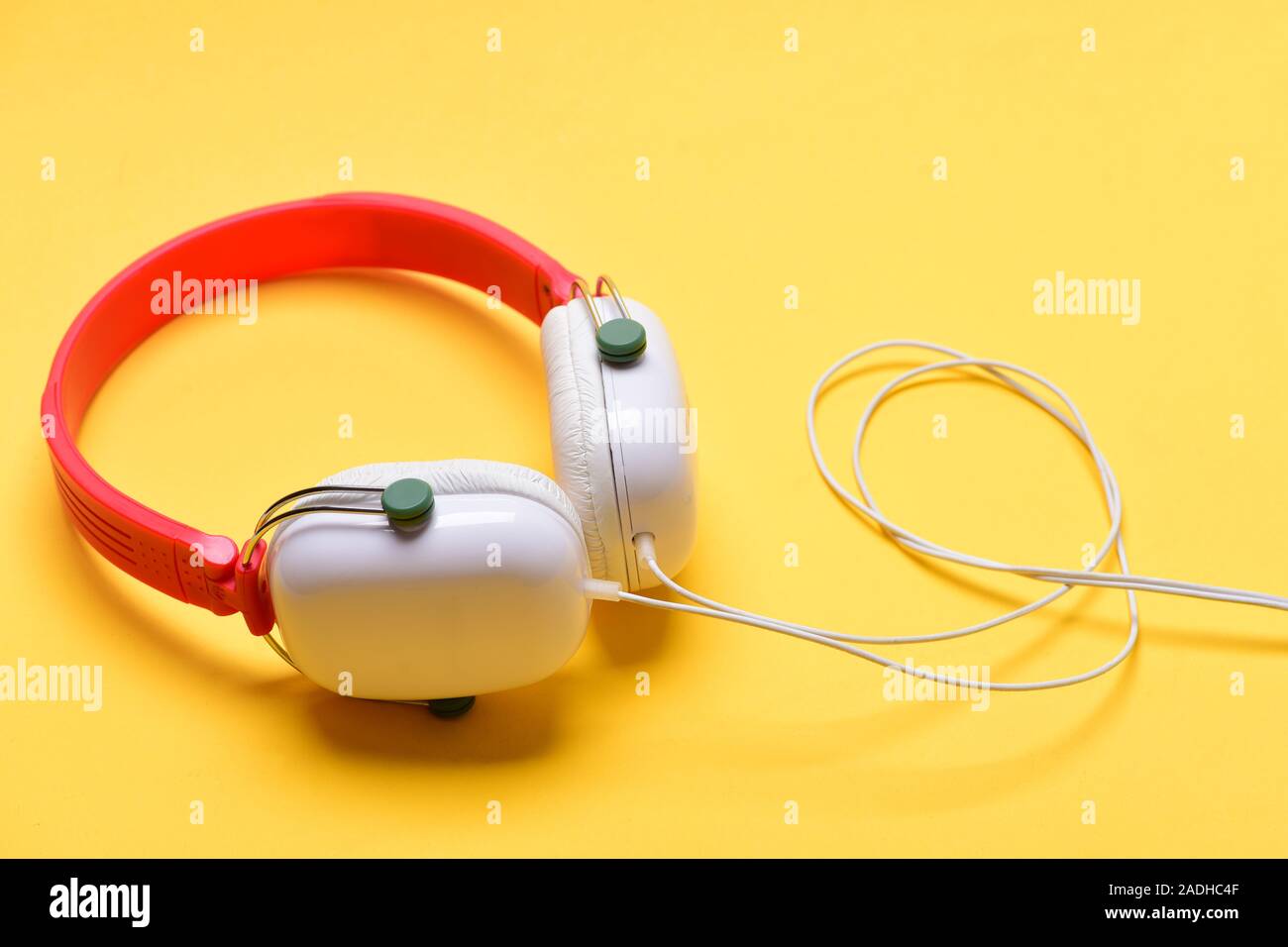 Auriculares en color blanco y rojo con cables largos. Auriculares para  música hecha de plástico. Auriculares modernos y elegantes sobre fondo  amarillo cálido. Accesorios de música y el concepto de tecnología Fotografía