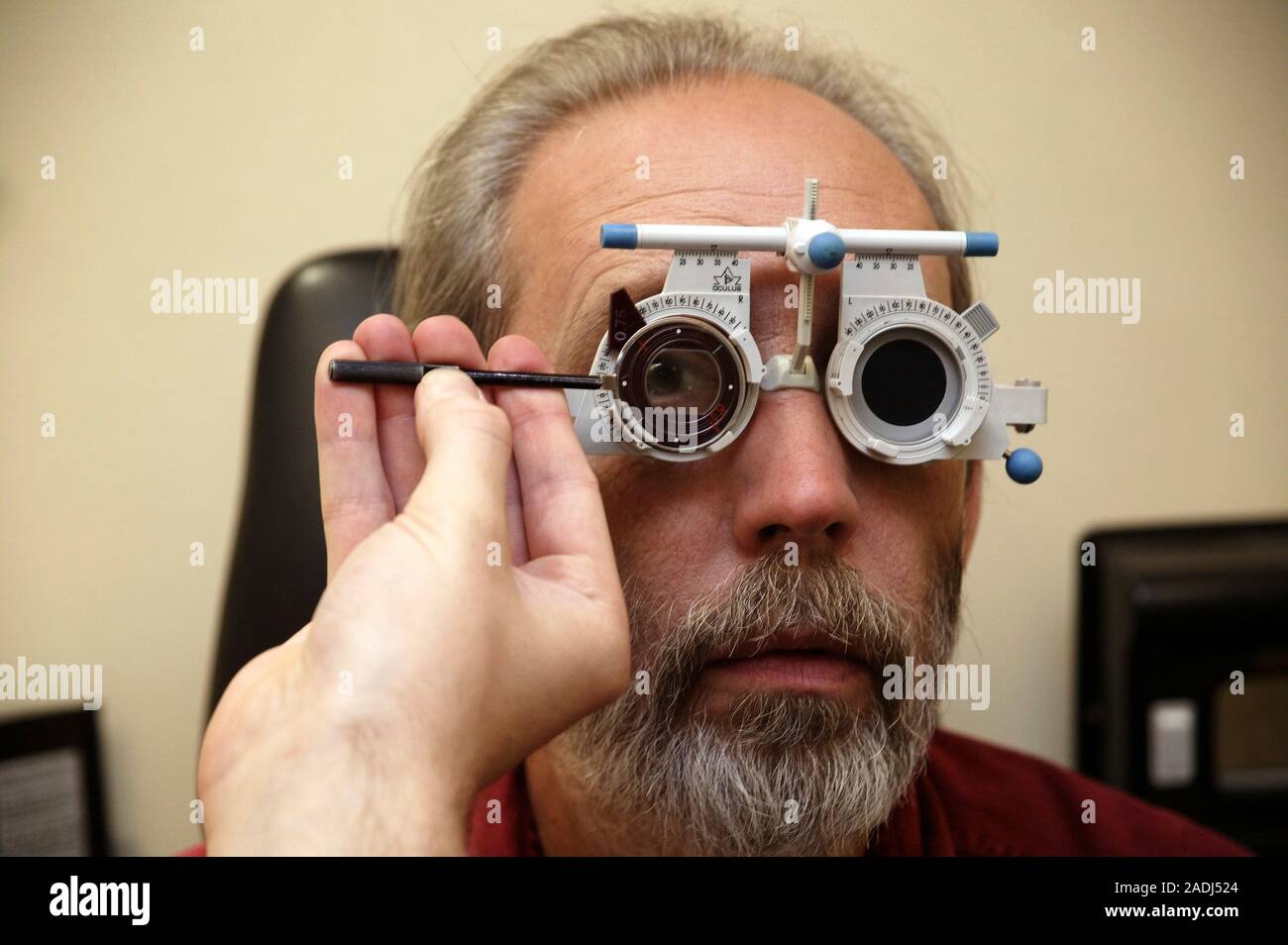 Hecho un desastre raíz Atravesar Prueba ocular. Hombre vestido con un conjunto de lentes ajustables durante  un examen ocular. La mano del optometrista es ajustar uno de los lentes. El  hombre está mirando Fotografía de stock -