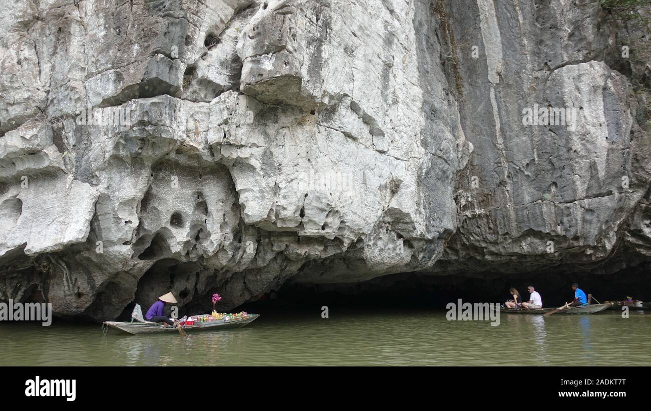 Una señora vende fruta de su barco mientras los turistas disfrutan de paseos en barco en una caverna bajo una montaña en Tam Coc en Ninh Binh, Vietnam Foto de stock