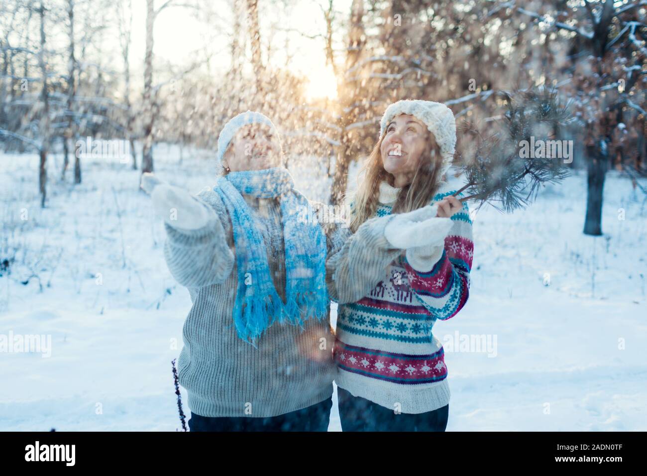 Divertidas actividades de invierno. Madre e hija adulta arrojar nieve afuera. Familia relajante en el bosque para vacaciones Foto de stock