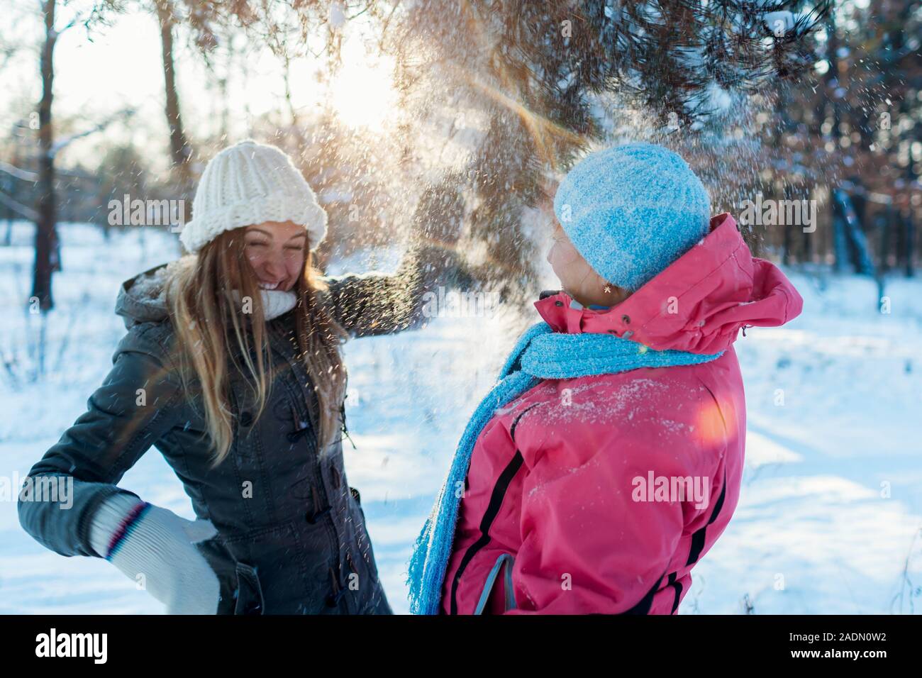 Divertidas actividades de invierno. Madre e hija adulta agitando ramas con nieve afuera. Familia de vacaciones relajantes Foto de stock