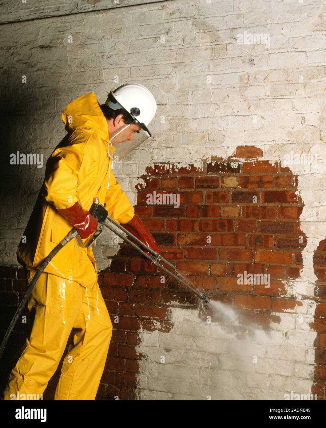 La eliminación de la pintura. Trabajador de la construcción con un chorro  de agua a alta presión para limpiar la pintura de una pared de ladrillo. Él  es el uso de ropa