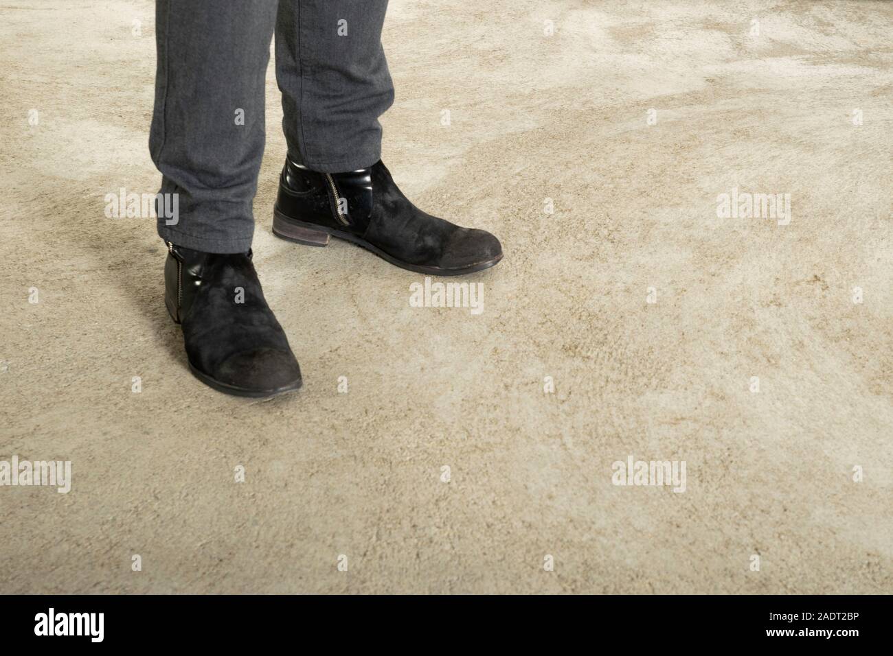 Hombre de pies en botas negras y pantalones de mezclilla oscuro sobre un  fondo de hormigón. Copia espacio para publicidad. El espacio negativo  Fotografía de stock - Alamy