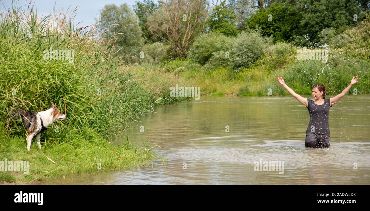 Mujer de pie en un lago, un perro joven en el Riverside, diversión en el verano camine, banner Foto de stock