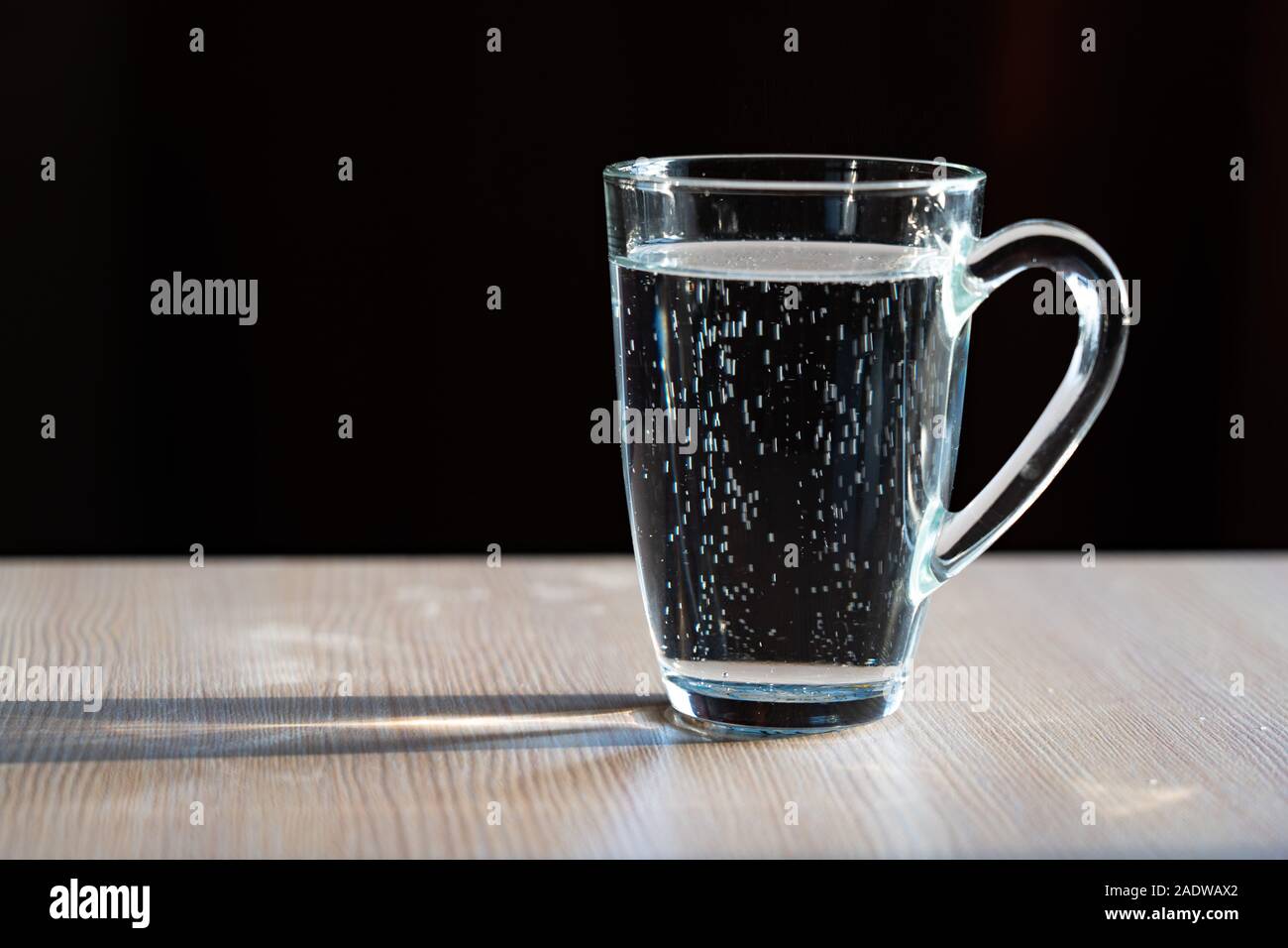 Vaso con agua sobre un fondo negro. Suben burbujas. Una jarra de vidrio  llena de agua se asienta sobre una mesa de madera. Una taza de agua  Fotografía de stock - Alamy