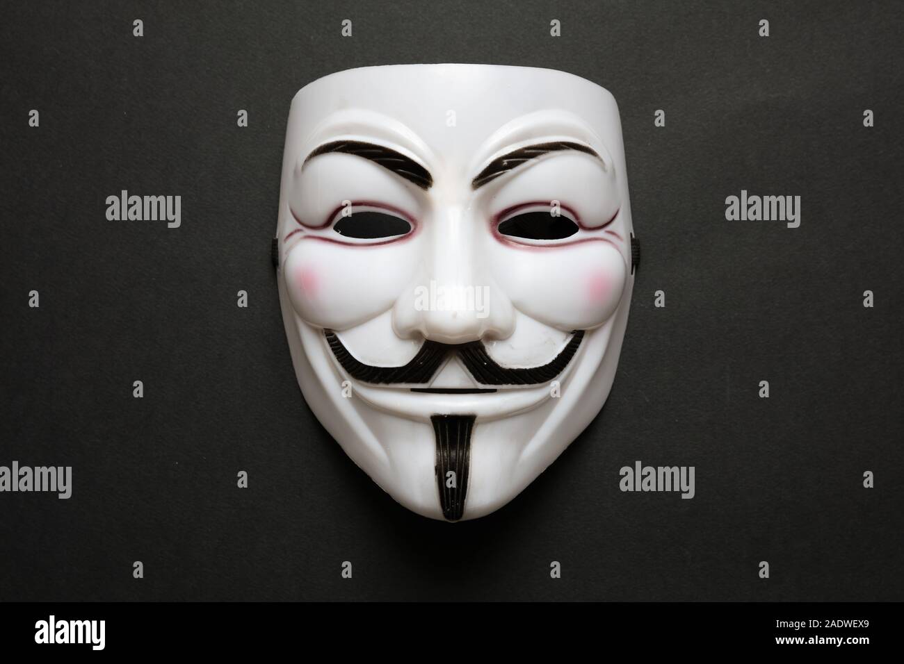 Vendetta máscara facial símbolo del grupo acktivist online anónimo contra el fondo negro, acercamiento. Foto de stock