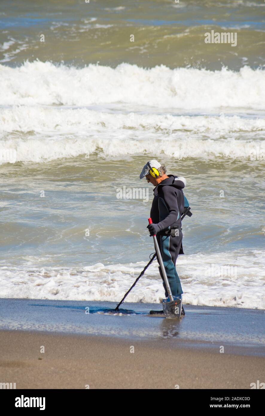 Hombre en wet suit buscando en la playa con el detector de metales, España. Foto de stock