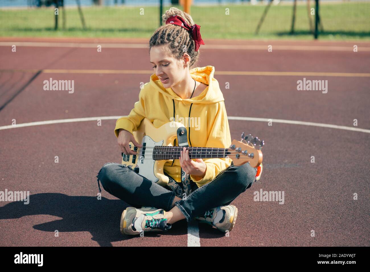 Bella Dama con dreadlocks tocando la guitarra y mirando inspirado Foto de stock