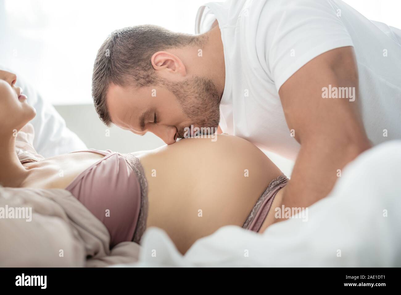 Abrazos y besos marido vientre de su esposa embarazada en la cama Foto de stock