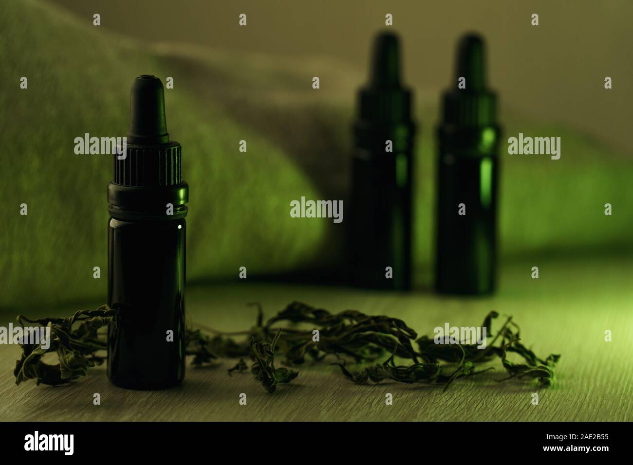 Composición horizontal de tres botellas de vidrio de 10 ml negro rodeado con hierbas secas sobre mesa de madera blanca con una luz verde retroiluminado Foto de stock
