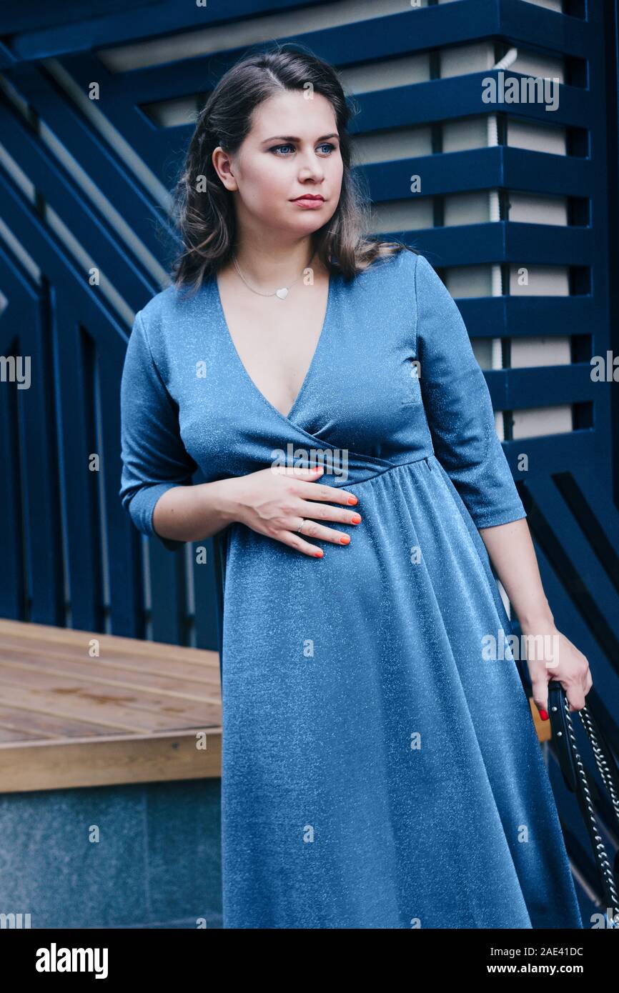 Hermosa joven de pelo rubio mujer embarazada de pie en elegante vestido azul de - Alamy