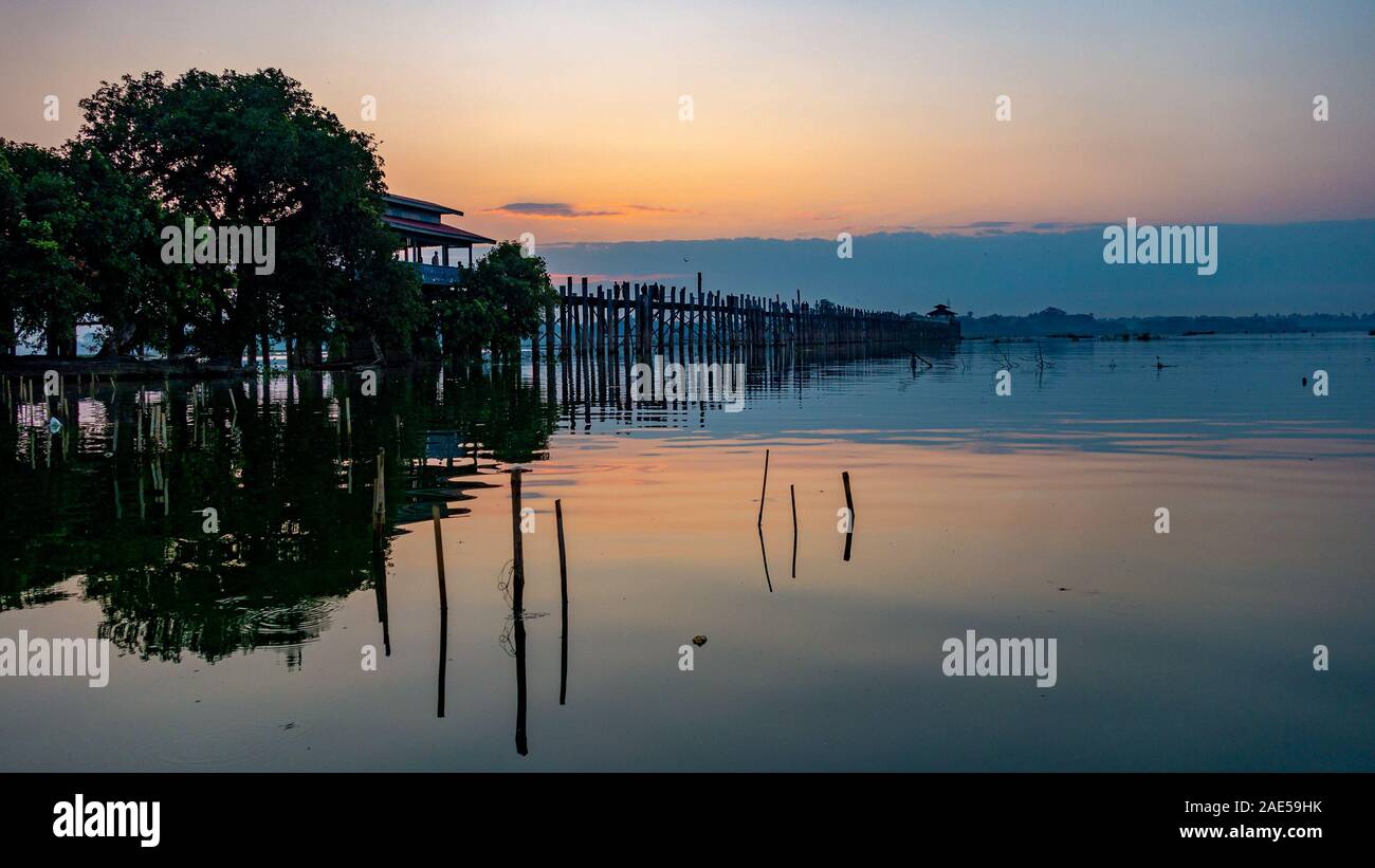 Vista del amanecer de los antiguos de madera de teca, U Bein Puente que cruza el lago Taungthaman en Amarapura, cerca de la ciudad de Mandalay en Myanmar (antigua Birmania) llamado Foto de stock