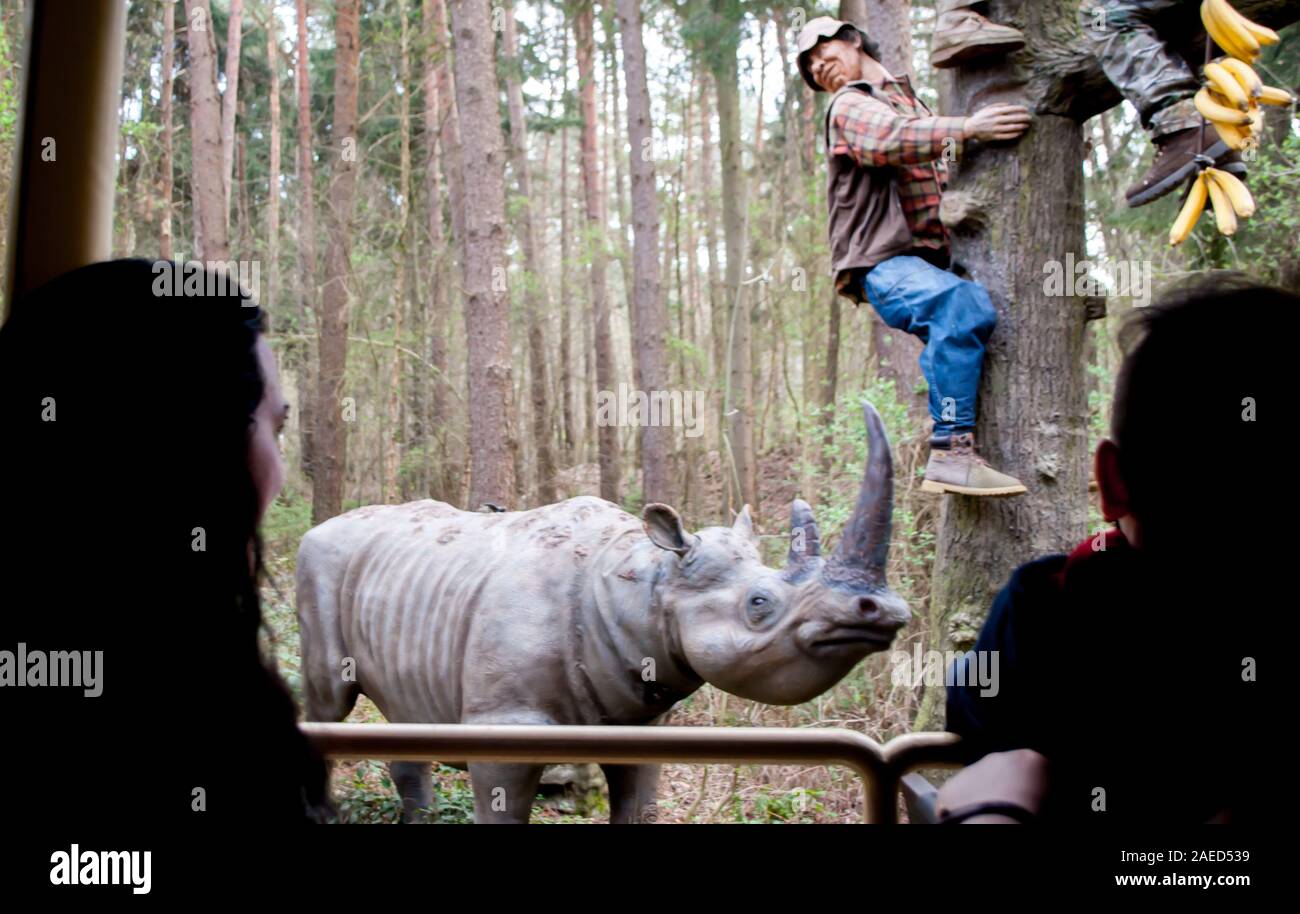 Hodenhagen, Alemania, 30 de marzo de 2019: Los modelos de un hombre huyendo de un rinoceronte en un árbol en un bosque en un zoológico Foto de stock