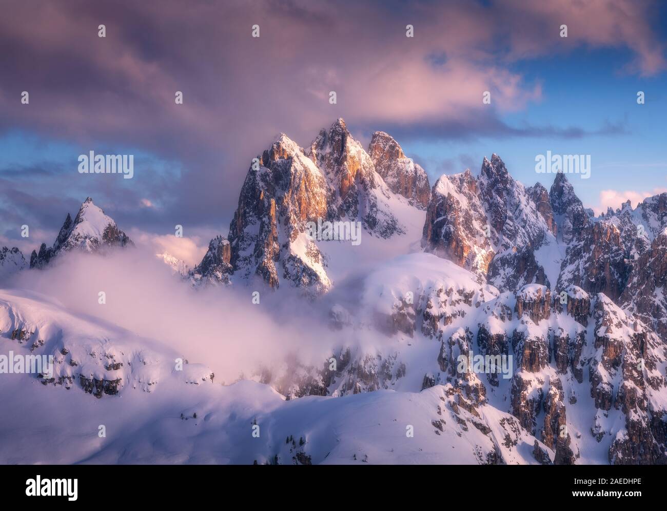 Picos montañosos nevados en niebla y cielo azul con nubes al atardecer Foto de stock