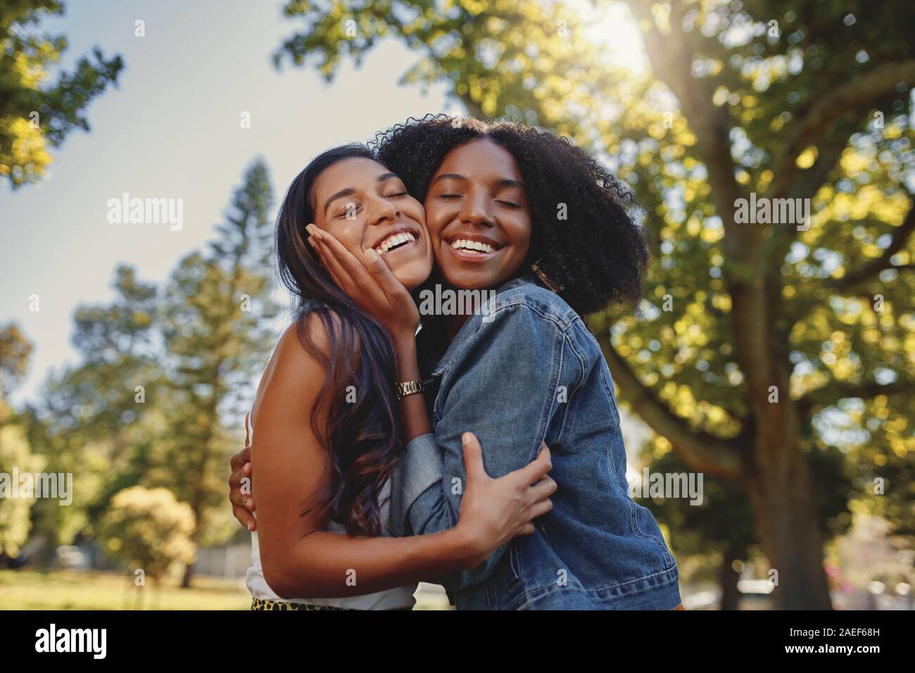 Sonriente, feliz retrato de una joven de diferentes amigas blanco y negro abrazando a cada uno de otros y divertirse al aire libre en el parque Foto de stock