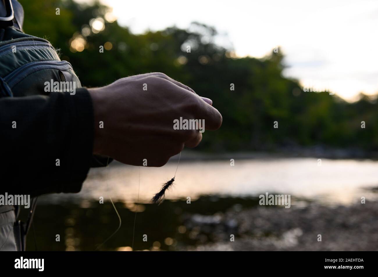 Una mano sujetando una mosca en un río al atardecer Foto de stock