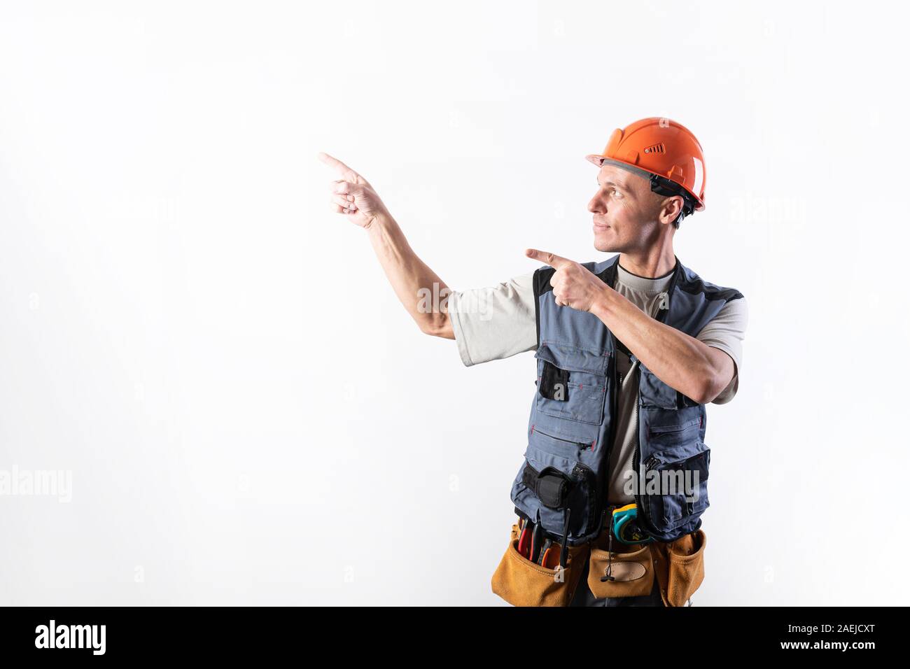 El constructor señala a la izquierda. Ofertas con los dedos índice. En ropa de trabajo y sombrero duro. Foto de stock