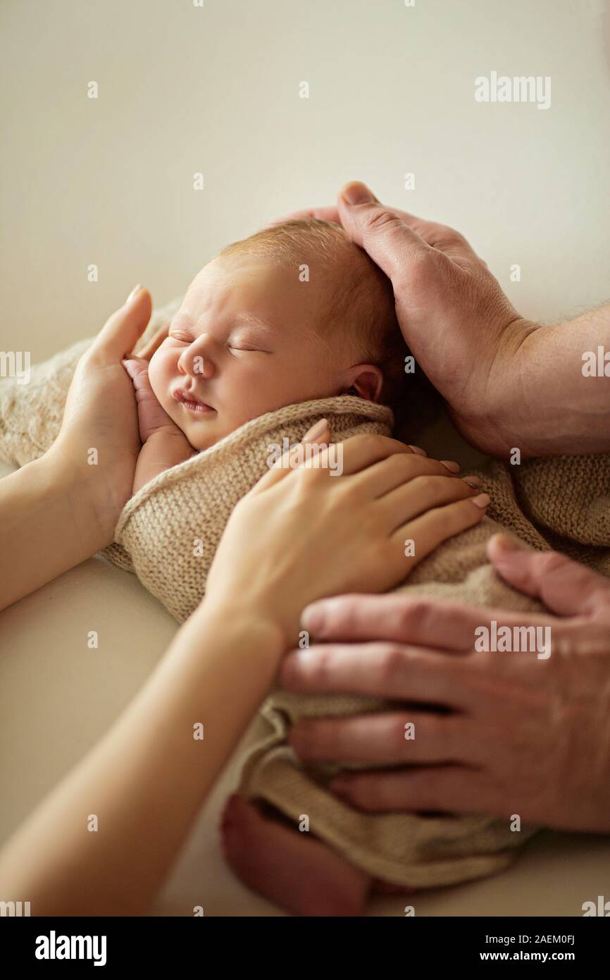 Lindo bebé niña acostada sobre su padre y madre manos, en casa Foto de stock