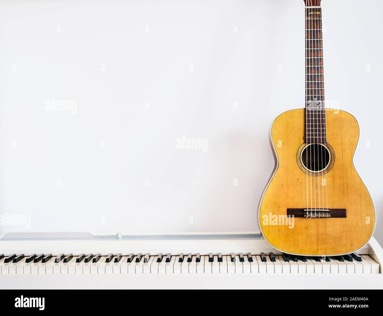 Guitarra acústica en el teclado del piano en frente de la pared blanca.  Instrumento de música de fondo Fotografía de stock - Alamy